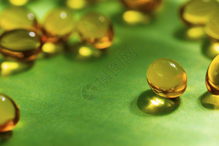 胶囊中的维生素在绿色背景上呈黄色特写维生素和矿物质缺乏对身体健康的概图片