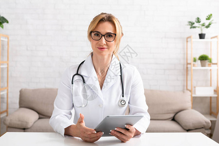 戴眼镜和白大衣的女医生手里拿着数字平板电脑图片