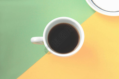 绿色和黄色背景的白色杯子和茶碟中的黑咖啡分为两部分图片