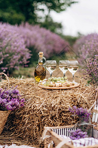在薰衣草丛中的干草堆上放着一杯酒一个野餐篮小吃和一束鲜花图片