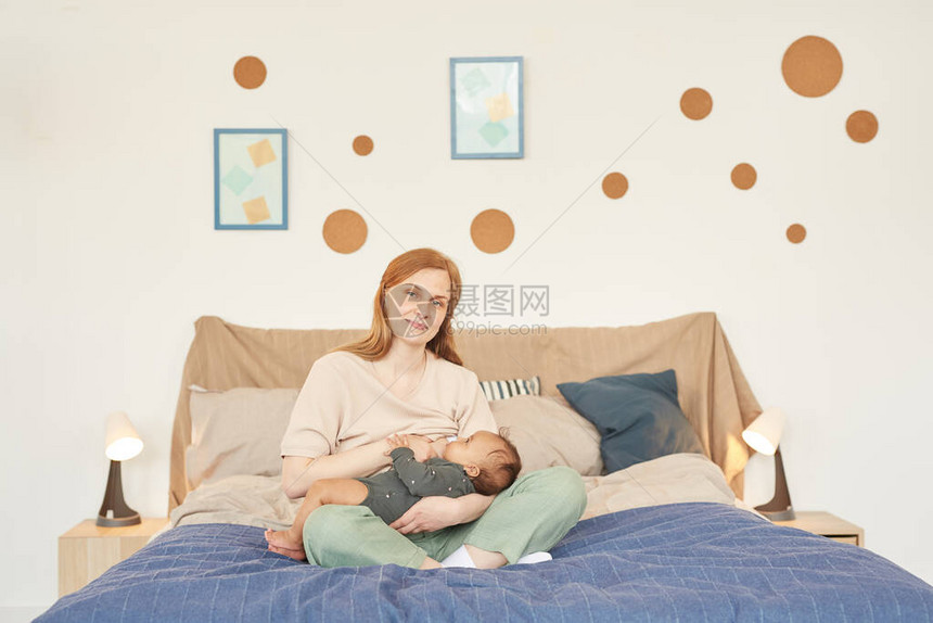 快乐成年母亲乳育婴双胞胎婴儿和坐在家中的床上看照相机复制空间全长的温图片