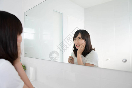 年轻的亚洲女在浴室镜子前刷牙时患牙痛蛀牙或敏感图片