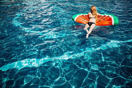 身穿黑色泳衣躺在水中游泳圈上的轻松苗条女人的背影照片图片