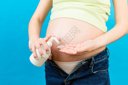 身穿无缝牛仔裤的孕妇用湿霜来防止腹部有长的伤痕图片