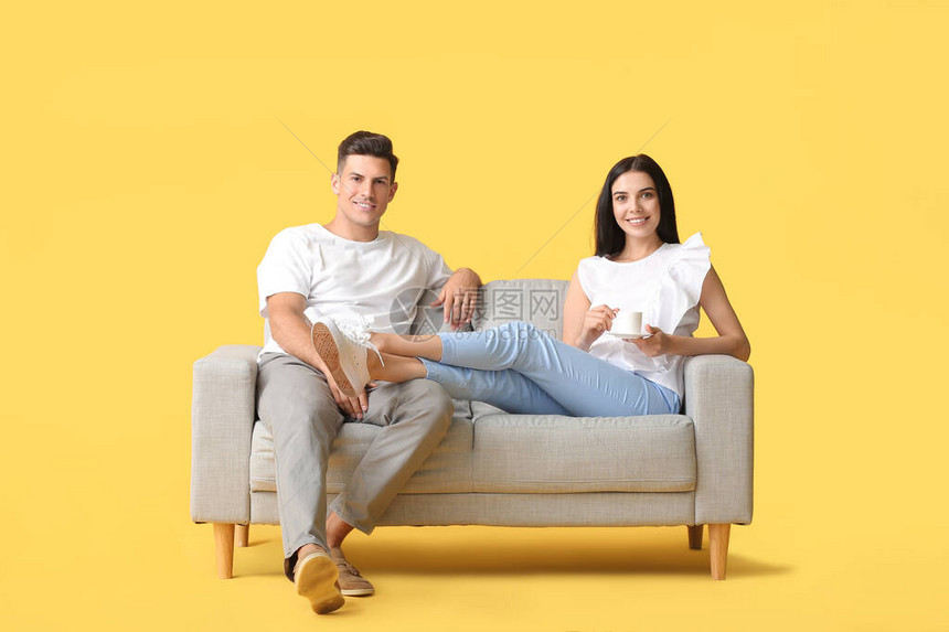 在彩色背景下在沙发上放松的年轻夫妇图片