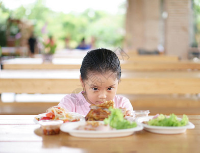 亚洲儿童可爱或小女孩喜欢吃看或盯着烤鸡配木瓜沙拉吃泰国菜图片