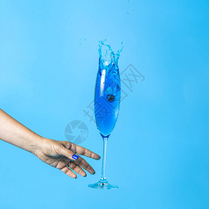 女人在蓝色背景上抓着蓝香槟的葡萄酒杯子图片