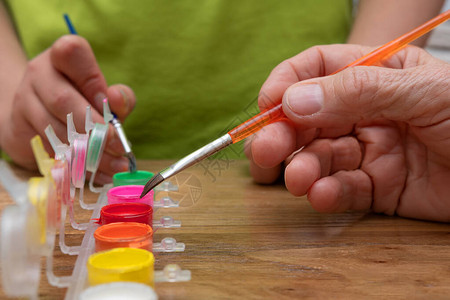 成人和儿童用手在木制桌上不同颜色的丙烯涂料罐中洗刷油漆笔迹嗜图片