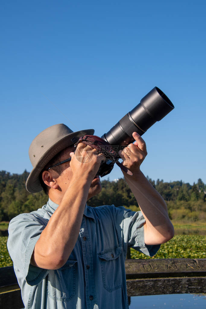 照片显示一位戴帽子和墨镜的亚洲男子将相机朝天空向上瞄准图片