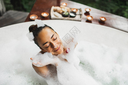 快乐的女人在泡大浴缸里玩泡沫在水疗中心放松图片