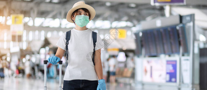 在机场航站楼戴面罩和手套持行李的年轻女旅客图片