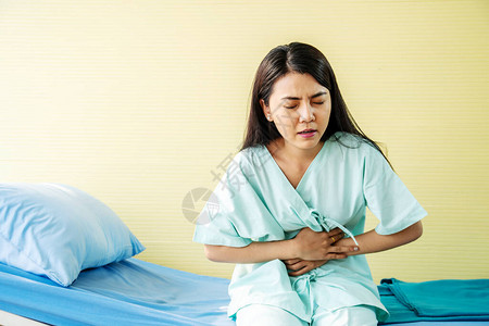 坐在医院床上腹部疼痛食物中毒时胃痛的女病人图片