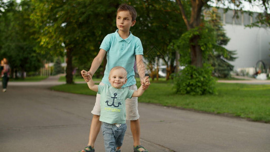 两个男孩在慢动作中去绿色公园轻松的母亲带着三个孩子在户外散步哥带着初图片