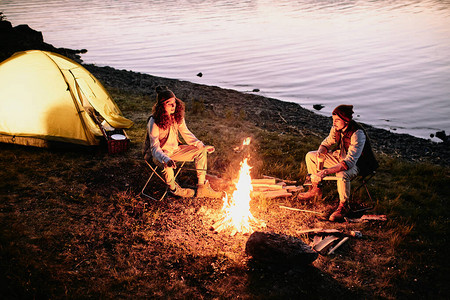 一对身着休闲装的年轻浪漫情侣坐在河岸的篝火旁图片