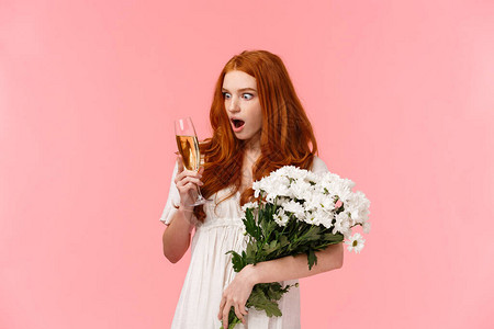 红发美女庆祝浪漫约会握着白色花束和酒杯粉红色背景图片