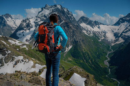 一位身穿蓝色衬衫背着橙色远足背包的年轻女游客欣赏壮丽的山景图片