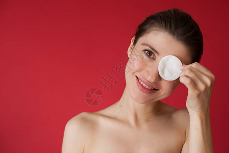 可爱的caucasian女人用雀斑遮住眼睛用棉盘蒙住她的眼睛在红图片