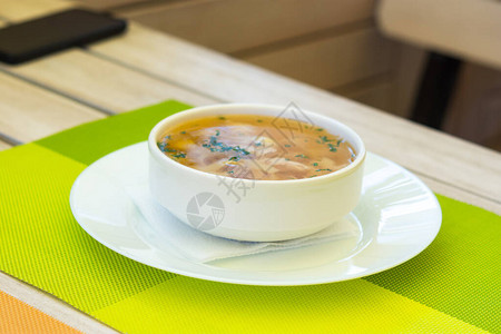 股票配资夏季咖啡馆的面条汤白色盘子里的黄汤这道菜的顶视图咖啡馆里的木制白桌健康的鸡汤配肉和面背景