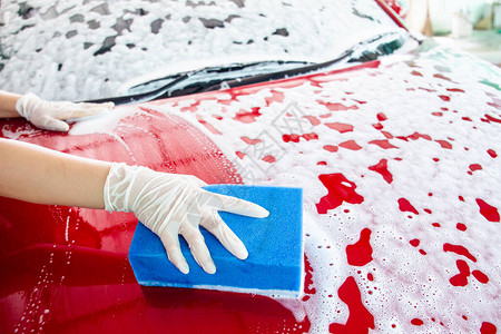 快乐美丽的亚洲女人用高压水和洗车海绵清洗她的现代红色汽车图片