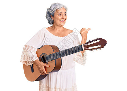 穿着灰色头发的高级女人弹着古典吉他把拇指向侧面用张图片