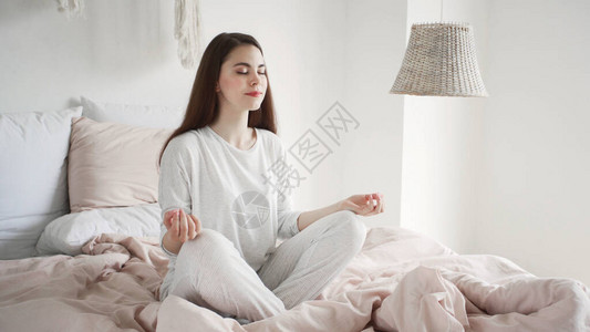 穿着睡衣的冷静而的年轻女子坐在舒适卧室的床上冥想背景图片