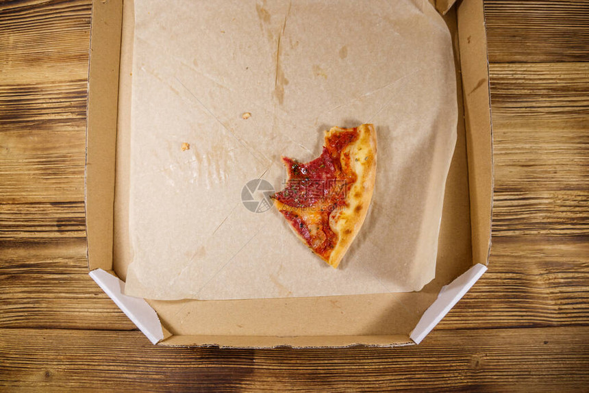在一张木桌上的纸板箱里咬了一片比萨饼顶视图送货上门的概念图片
