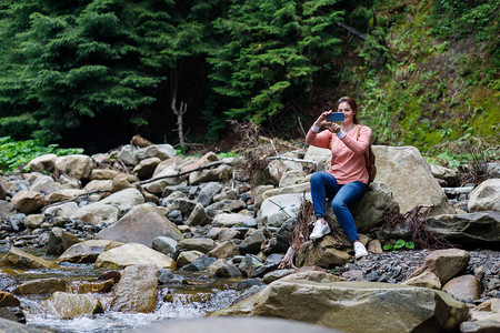 在山河背景的电话里女旅游者在石头上拍照片他写图片