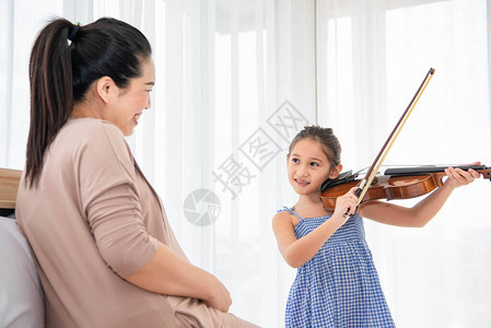 女孩与怀孕母亲一起为婴儿腹部的新生儿玩小提琴图片