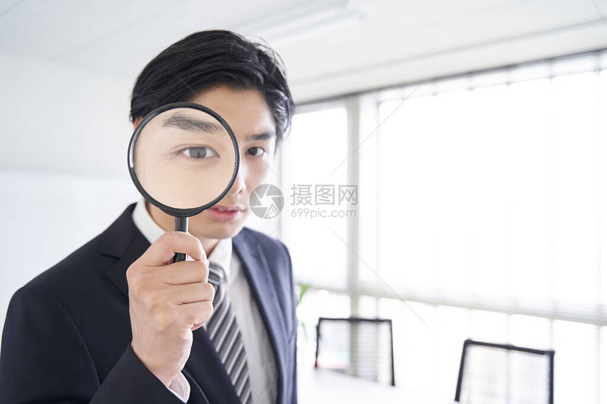 一位日本男商人在会议室里透过放大镜寻找图片