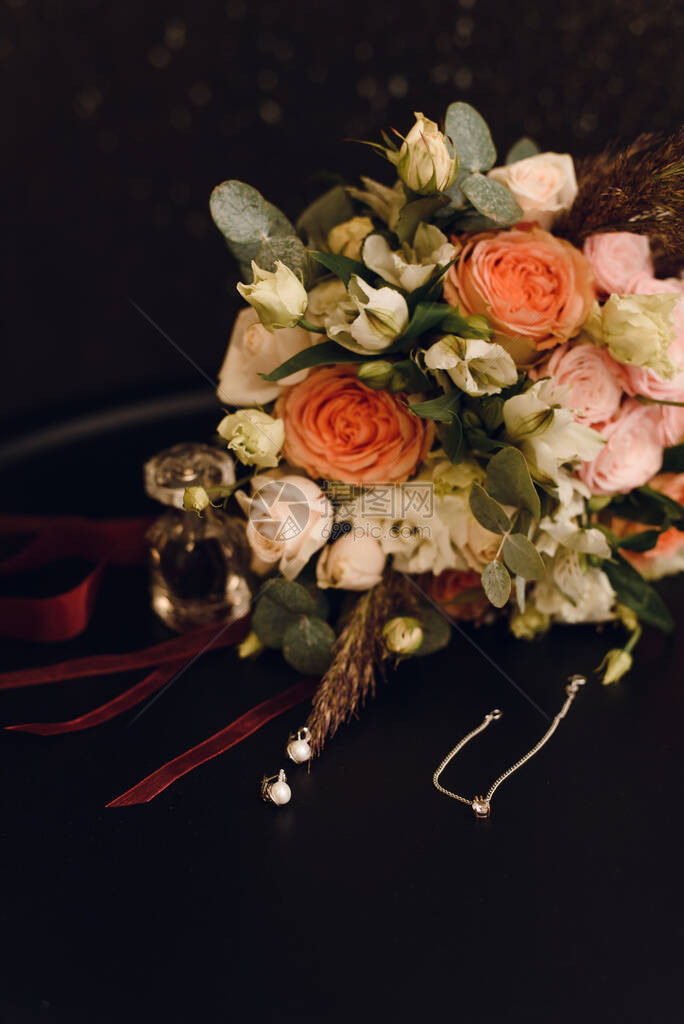 新娘首饰旁边的玫瑰花束婚纱和红天鹅绒上的耳环婚礼和爱情概图片