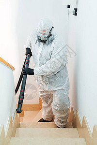 穿戴个人防护设备的人爬上从COVID19消毒的房屋楼图片