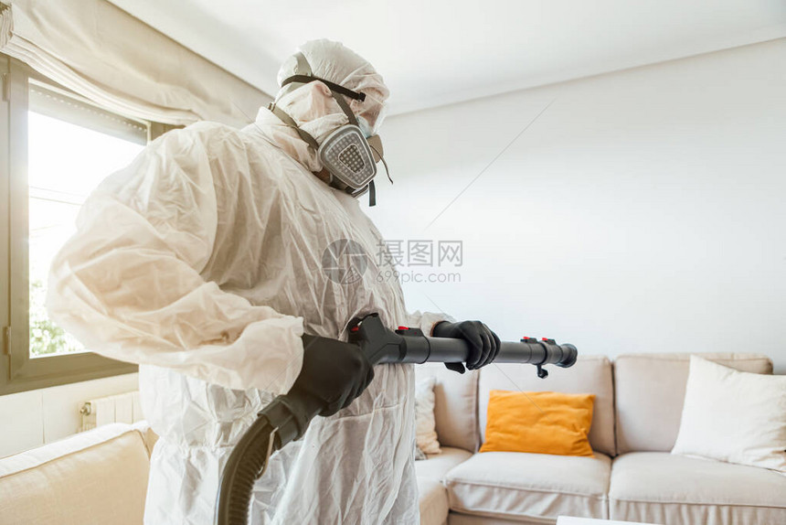穿着PPE的男子用COVID19消毒机对房子的客厅进行消毒大流行图片
