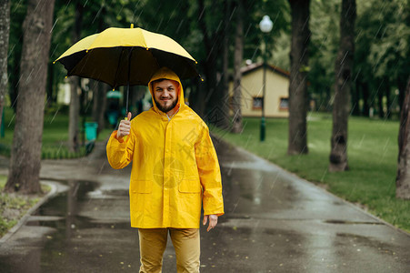 雨天打着伞走在夏日公园的男人雨披和橡胶靴的男图片