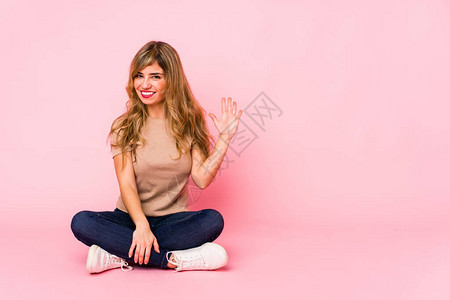 坐在粉红色工作室的金发美女笑着开心地展示五号手图片