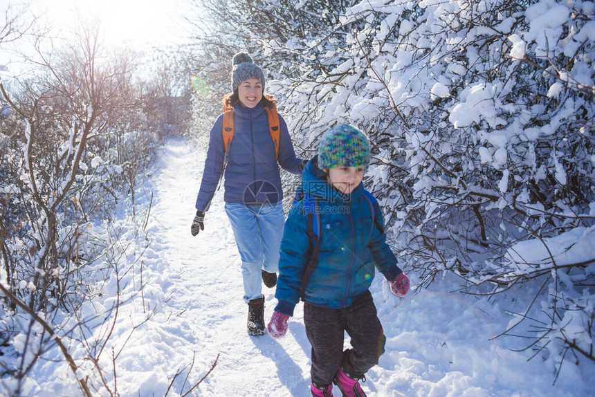 孩子从妈身边跑开一个女人带着孩子在冬季公园散步这个男孩花时间和他的母亲在一起母亲的爱穿过白雪皑的森图片