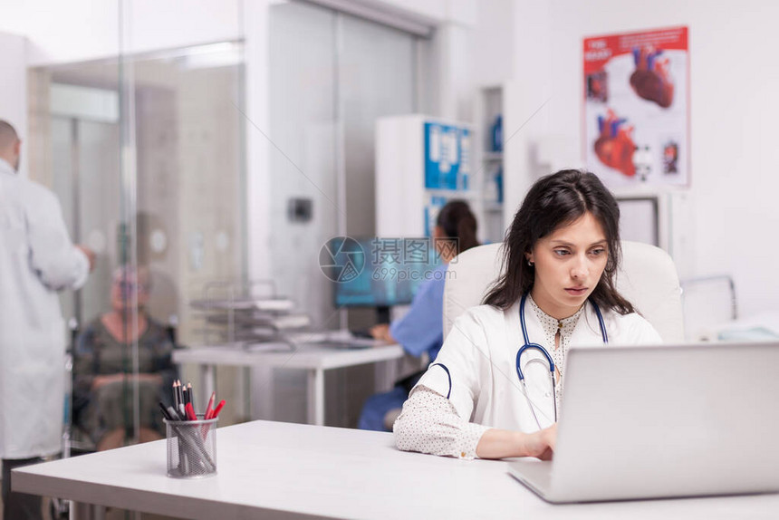 医院办公室的年轻医生在笔记本电脑上阅读关于治疗癌症的新药的报告残疾高级妇女在诊所走廊上与身穿白大图片