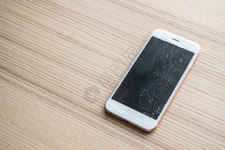 木制背景的破碎玻璃移动电话屏幕图片