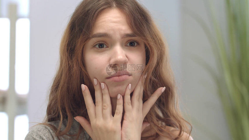 心烦意乱的少女看着问题皮肤和触摸脸前浴室镜子担心的年轻女人在浴室里抚摸皱纹黑斑的脸皮图片