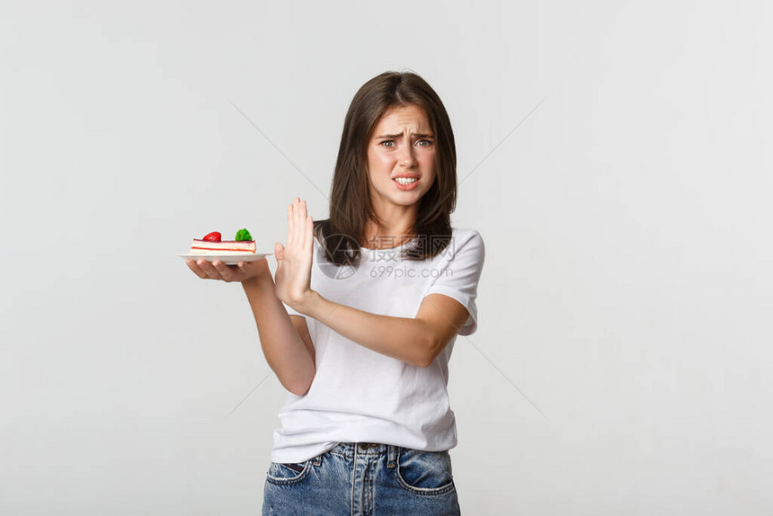 令人厌恶的年轻女子拒绝吃可怕的蛋糕做出拒绝姿态和图片