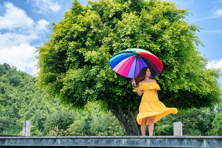 带着彩虹伞站在大树旁的年轻女子图片