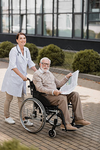 与残疾老年男子在户外报纸上散步时看相片的社工欢乐图片