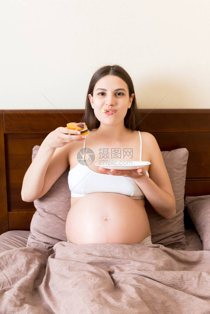 饿肚子的孕妇在床上放松时贪婪地吃着一块蛋糕图片