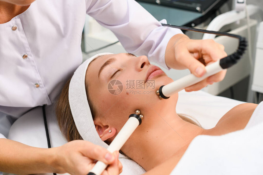 女在诊所的柜子里用滚筒做面部微流乳房刺激程序为坐在教练硬件现代美容学上图片