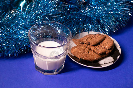 新年玩具和蓝底装饰品旁边的圣诞老人牛奶饼干和饼干图片