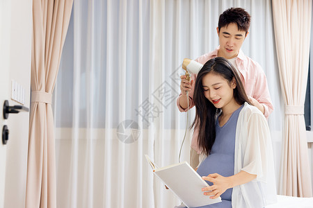 准妈年轻男士为怀孕的妻子吹头发背景