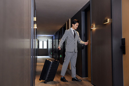 出差的商务男士手拉行李箱入住酒店酒店走廊高清图片素材