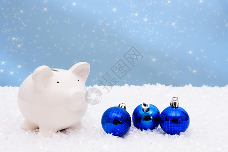 蓝圣诞钟和小猪银行在雪上和蓝背景图片
