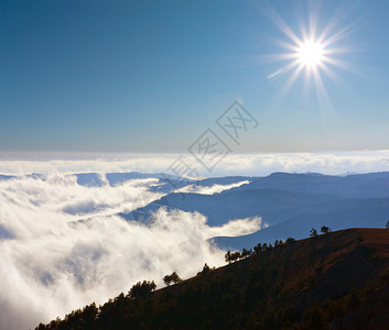 太阳在山脉上的云层上的山景图片