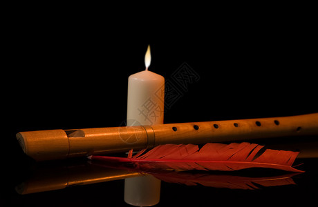 长笛燃烧的蜡烛和红色羽毛的静物图片