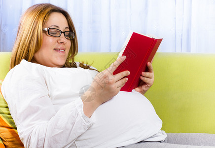 幸福的孕妇在家庭环境中阅读一本图片
